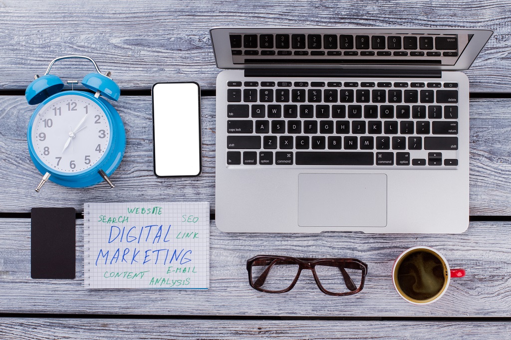 Digital marketing concept flat lay. Laptop with alarm clock and coffee cup.